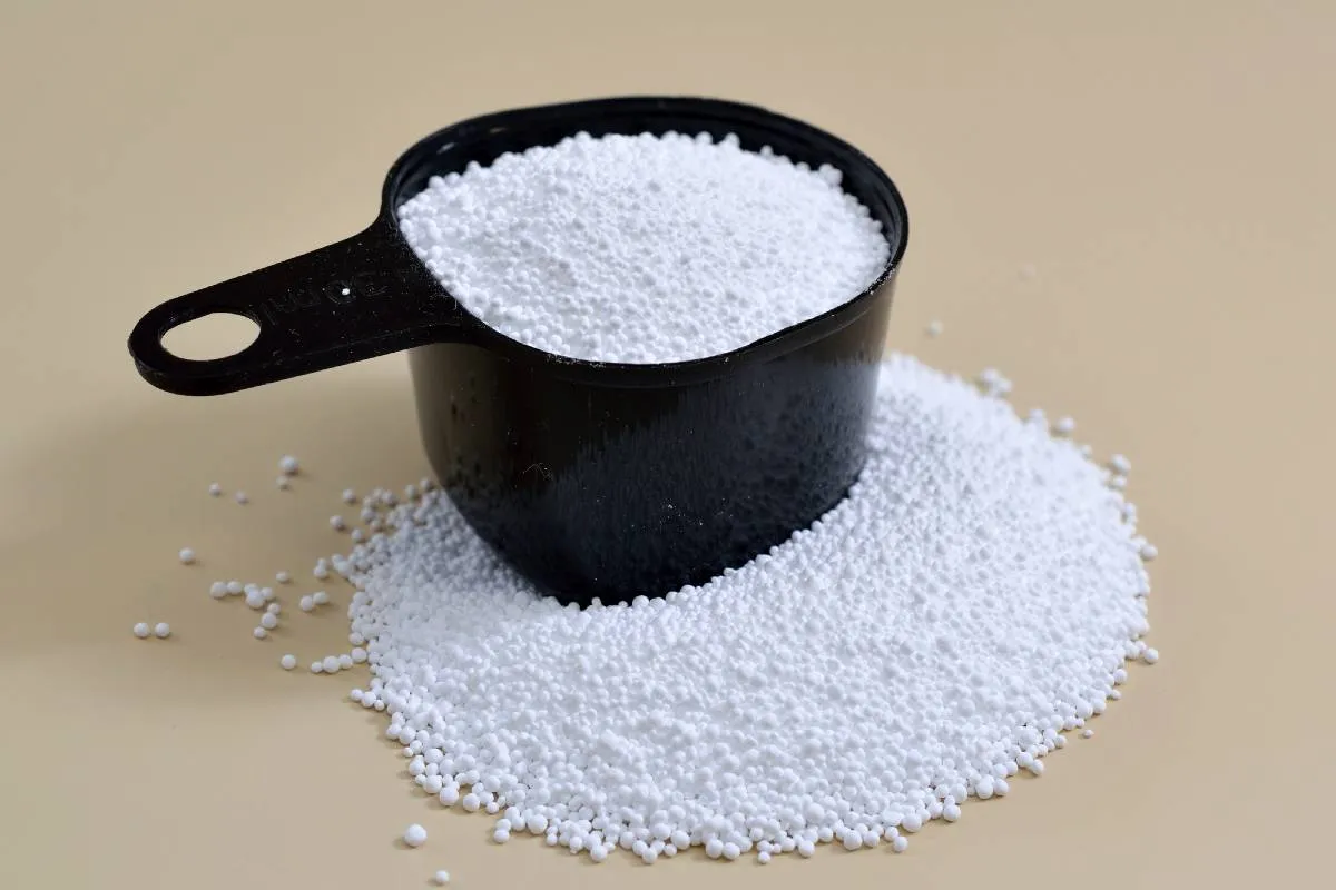 Imagem mostra um copo medidor com percarbonato de sódio em cima de uma mesa bege.