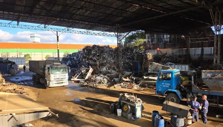 Reciclagem em Curitiba / barracão de recicláveis com caminhões e pilhas de metais no chão do barracão
