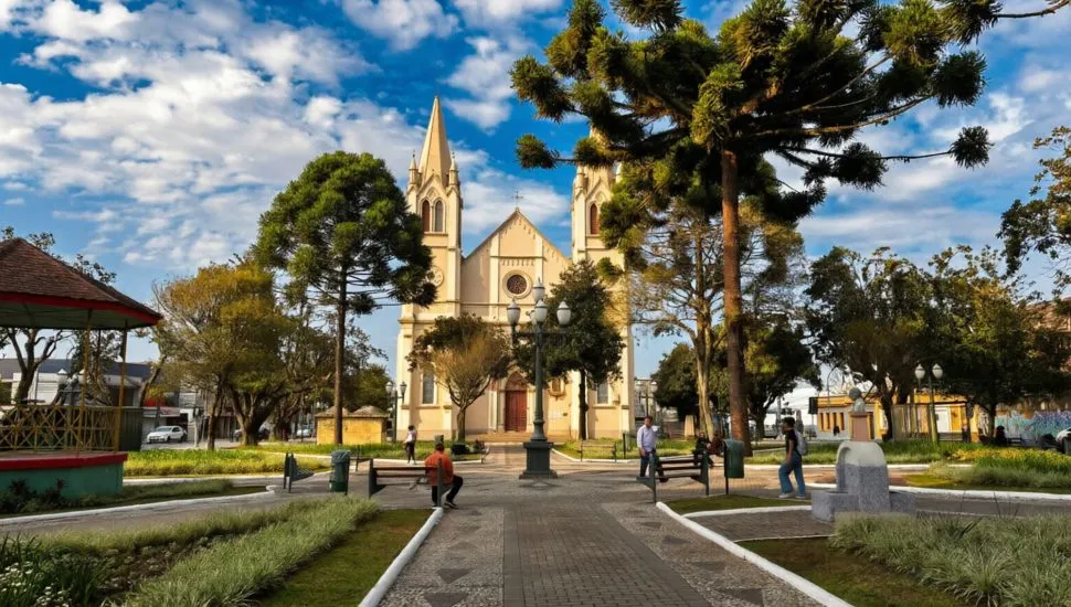 imagem mostra igreja principal da praça central de Campo largo com muitas árvores e araucárias