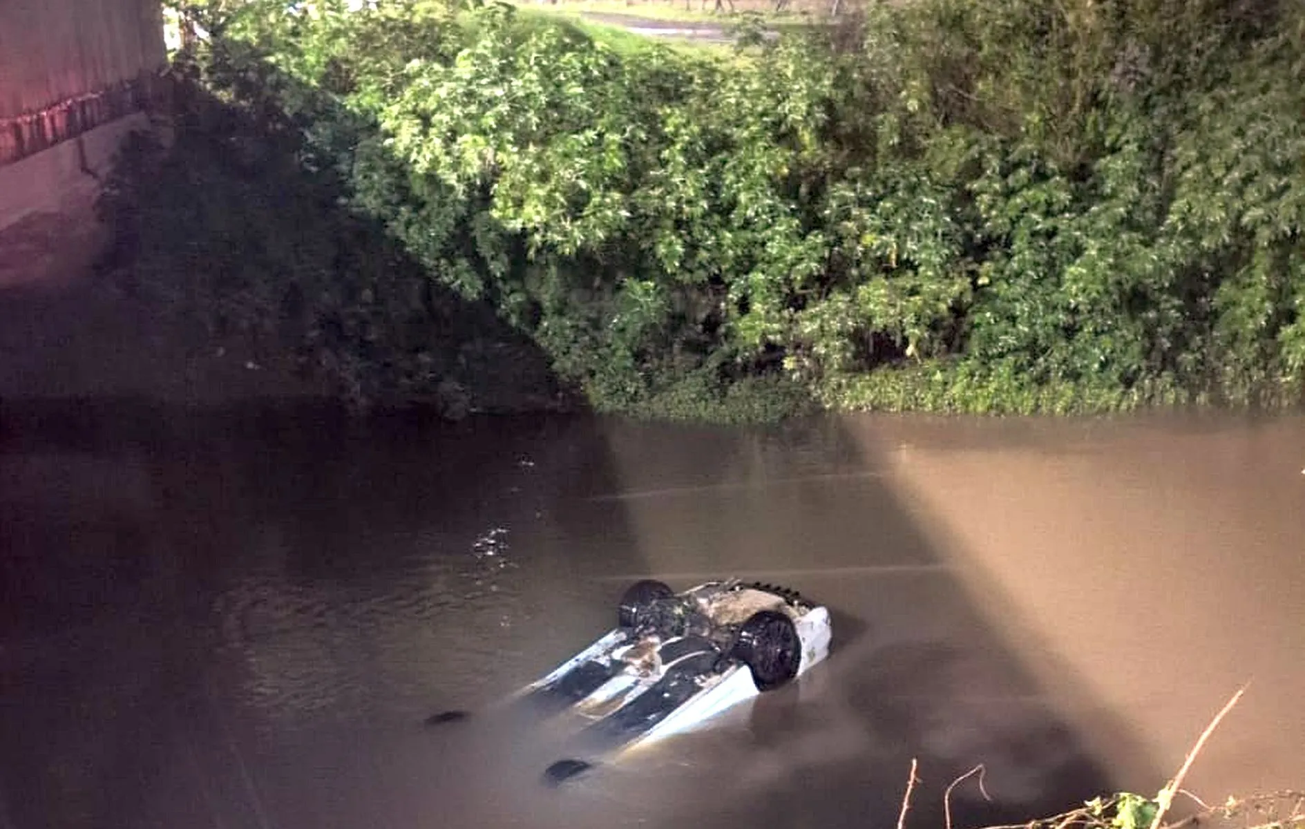 Imagem mostra carro de ponta cabeça dentro de um rio, parcialmente submerso