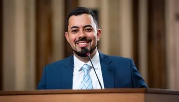 na imagem, um homem discursa em uma tribuna em uma casa legislativa.