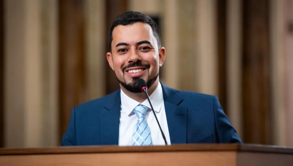 na imagem, um homem discursa em uma tribuna em uma casa legislativa.