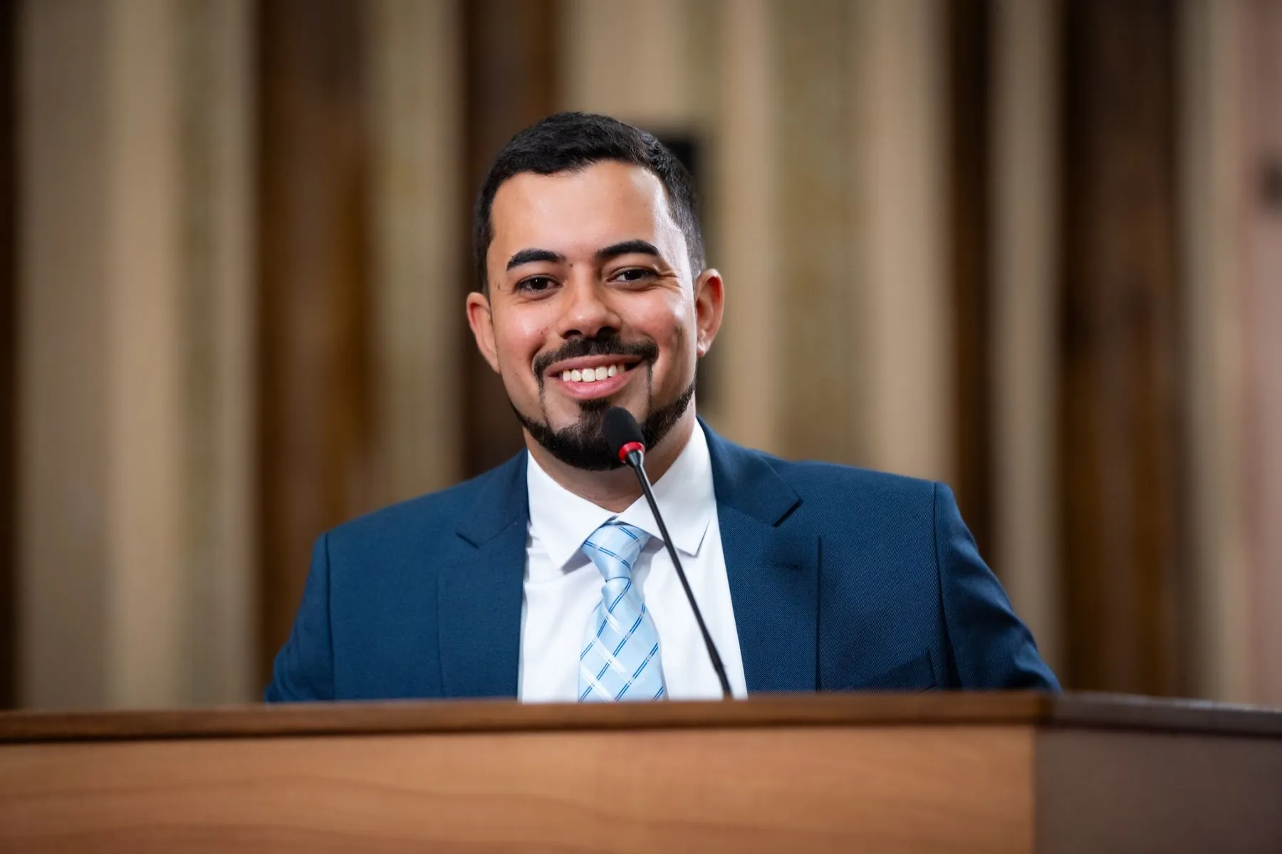 na imagem, um homem discursa em uma tribuna em uma casa legislativa.