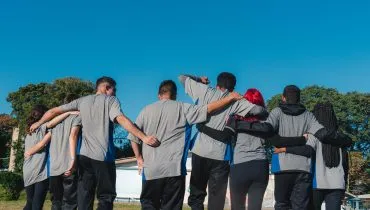 A imagem mostra um grupo de estudantes paranaenses de costas, caminhando abraçados.