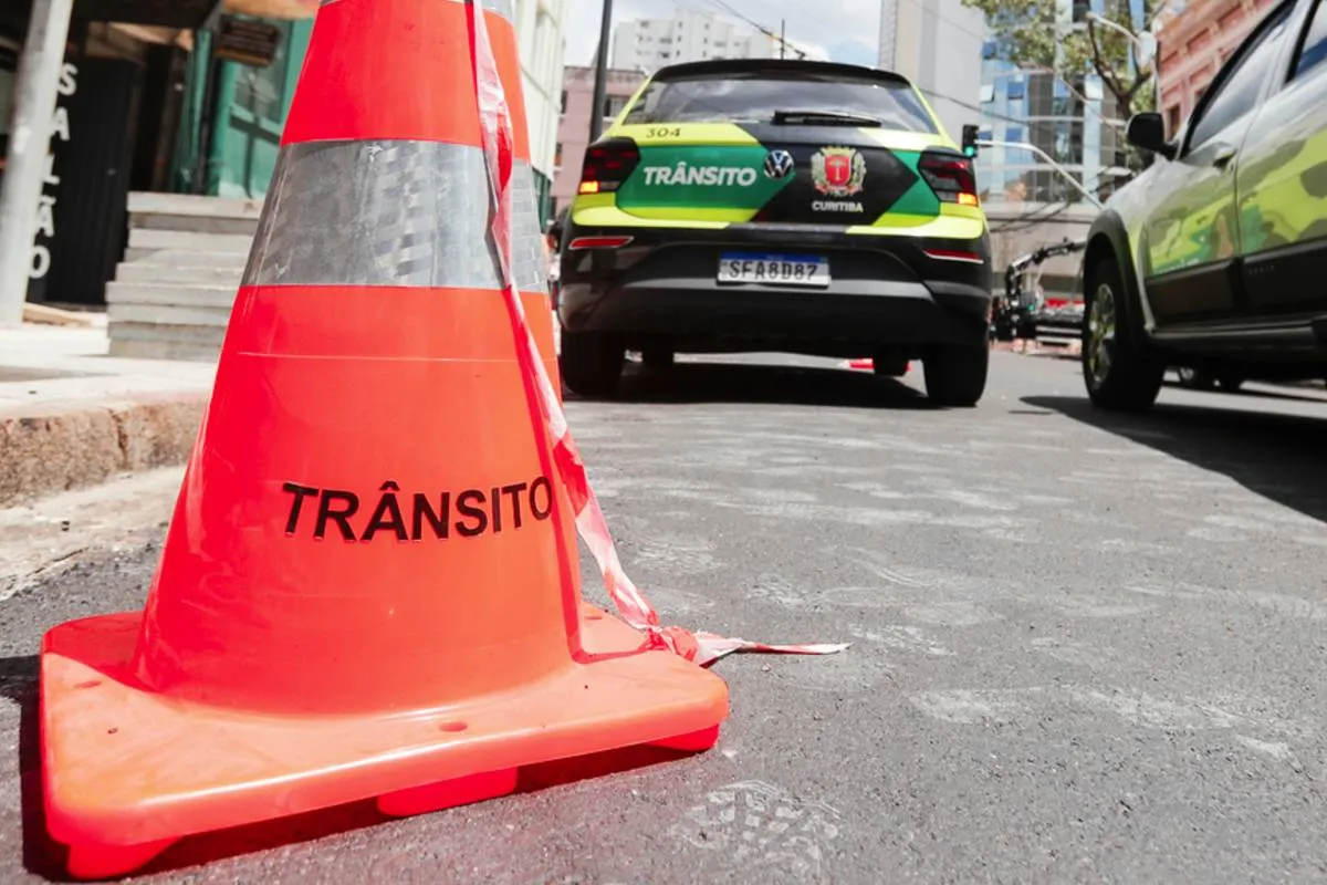 Imagem mostra um cone de trânsito atrás de uma viatura verde da Setran em uma rua de Curitiba.