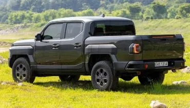 Imagem mostra a Kia Tasman, com destaque para a lateral e traseira da nova picape, estacionada em um campo com montanhas.