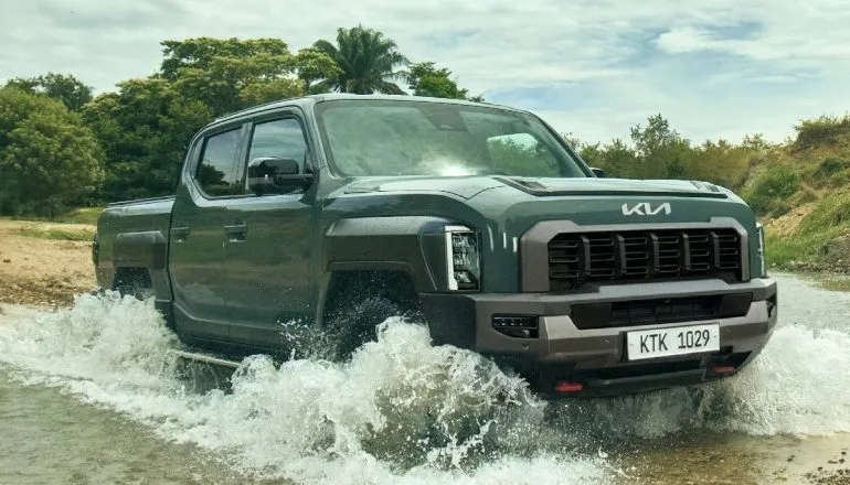 Imagem mostra a Kia Tasman passando em um rio, com detalhe para a grande grade frontal do modelo.