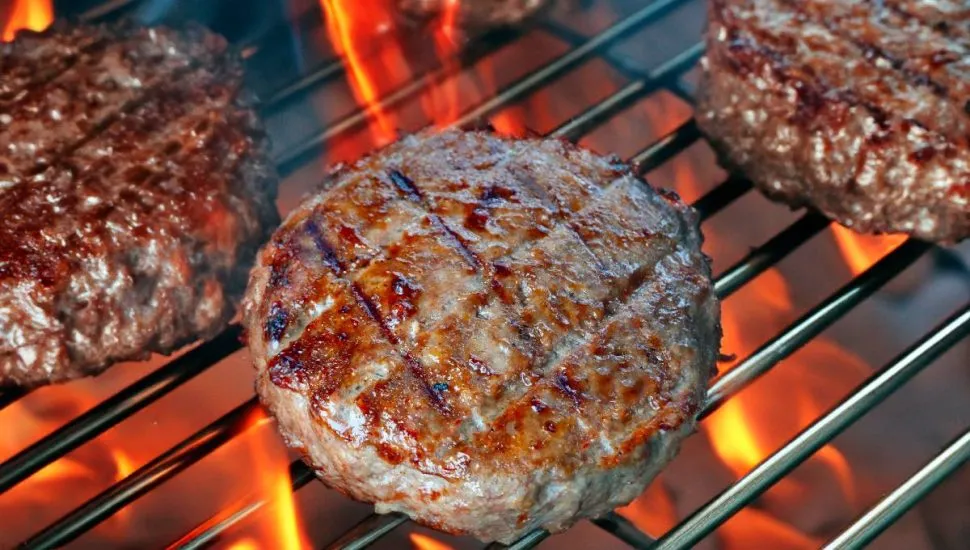 Imagem mostra um hamburguer sendo grelhado no fogo.