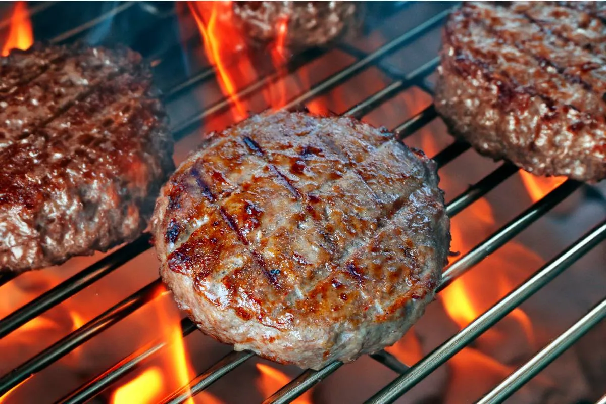 Imagem mostra um hamburguer sendo grelhado no fogo.