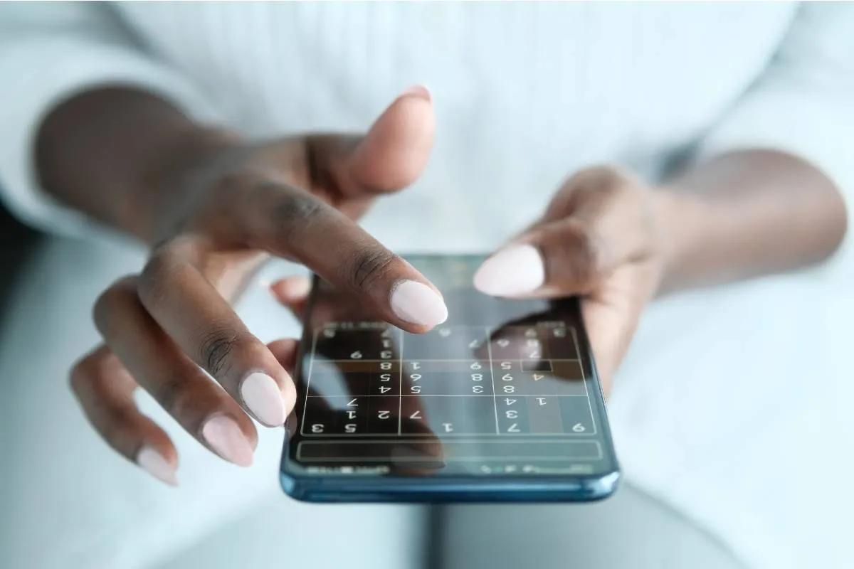 Imagem mostra uma mulher jogando Sudoku online pelo celular.