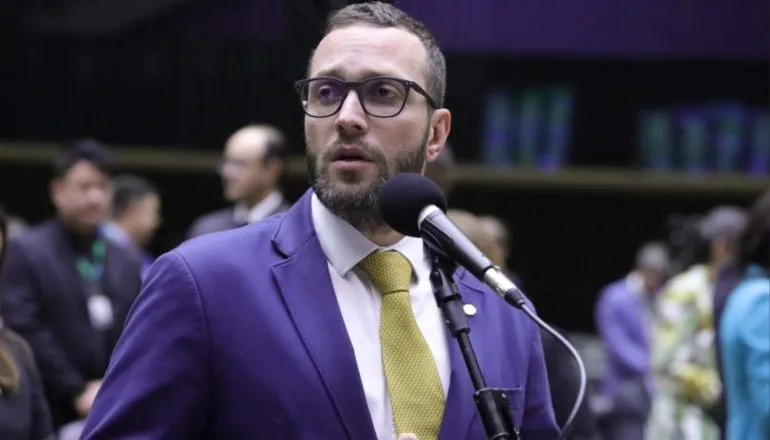 A imagem mostra o deputado federal Filipe Barros na Câmara dos Deputados, falando ao microfone.