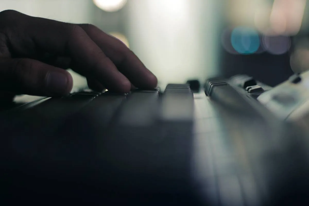 Imagem mostra o detalhe de uma pessoa usando um computador. O foco da imagem está nos dedos em cima do teclado.