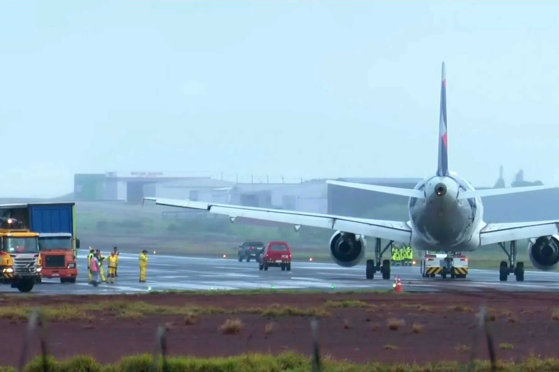Imagem mostra um avião em uma pista de aeroporto com veículos de apoio e operários ao lado.