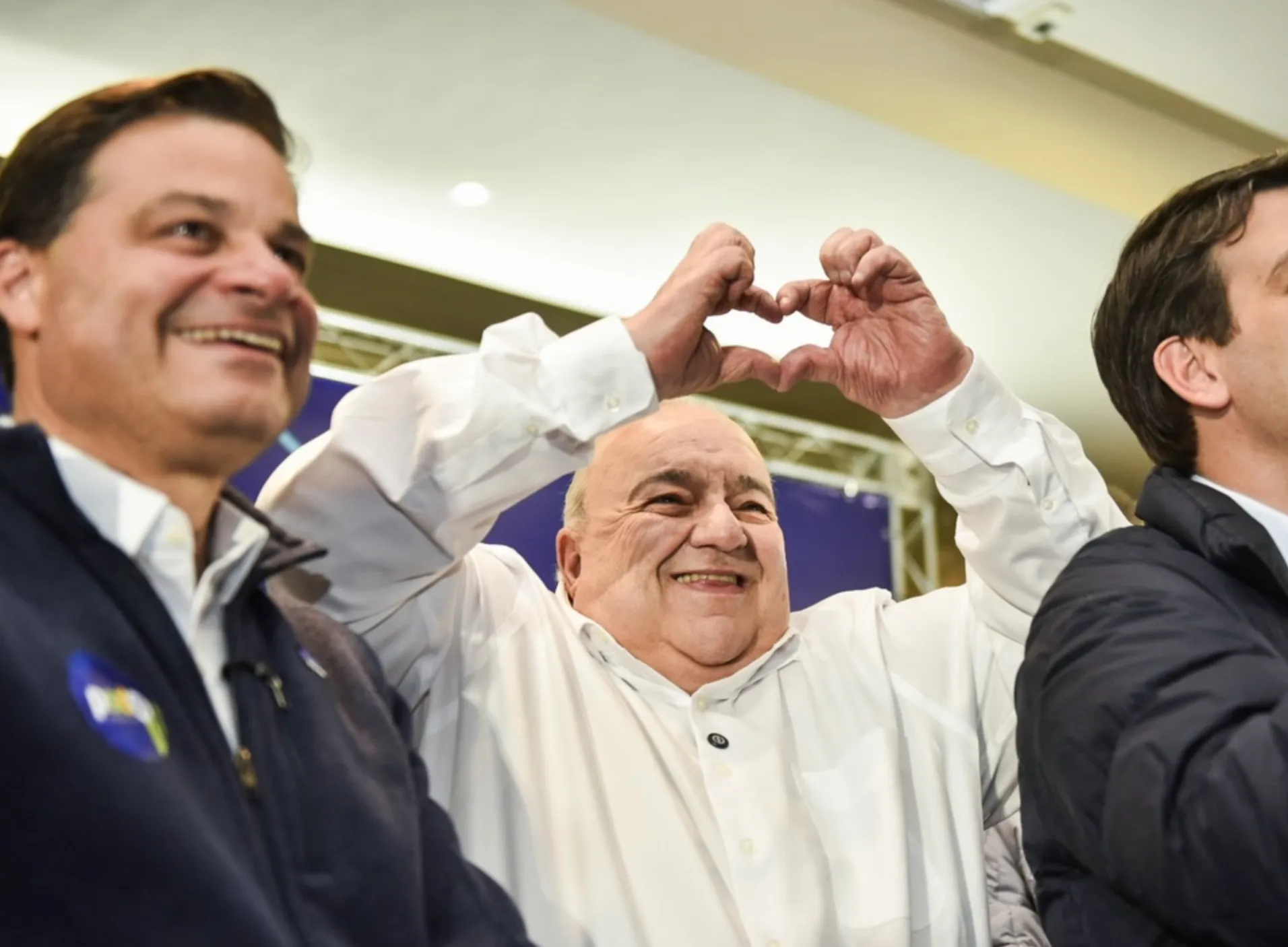 A imagem mostra Rafael Greca fazendo um coração com as mãos. Ao lado dele está Sandro Alex.