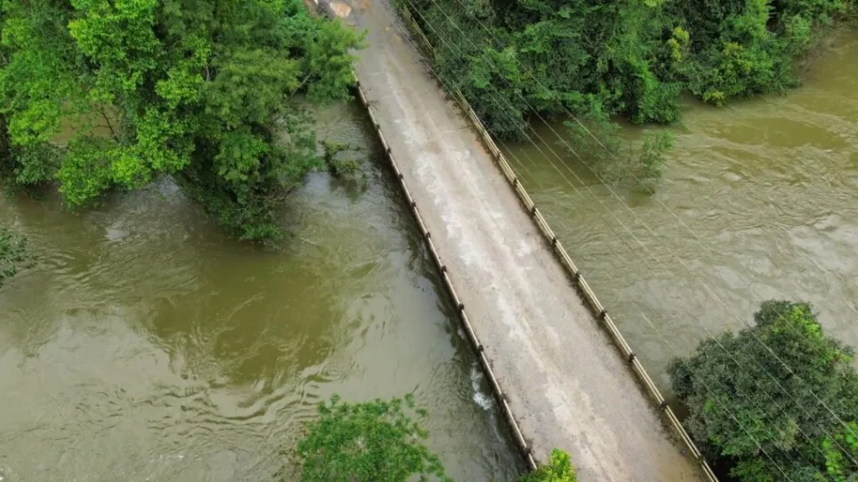 A foto mostra uma ponte quase coberta pela água do rio, de cor turva