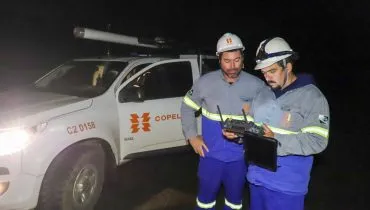 A imagem mostra dois servidores da Copel segurando equipamentos. Ao fundo está uma camionete da companhia.