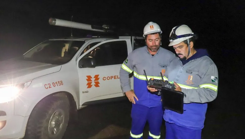 A imagem mostra dois servidores da Copel segurando equipamentos. Ao fundo está uma camionete da companhia.