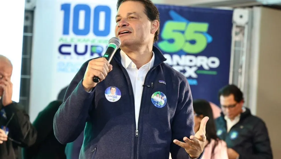A imagem mostra o candidato Sandro Alex falando ao microfone durante ato de sua campanha eleitoral.
