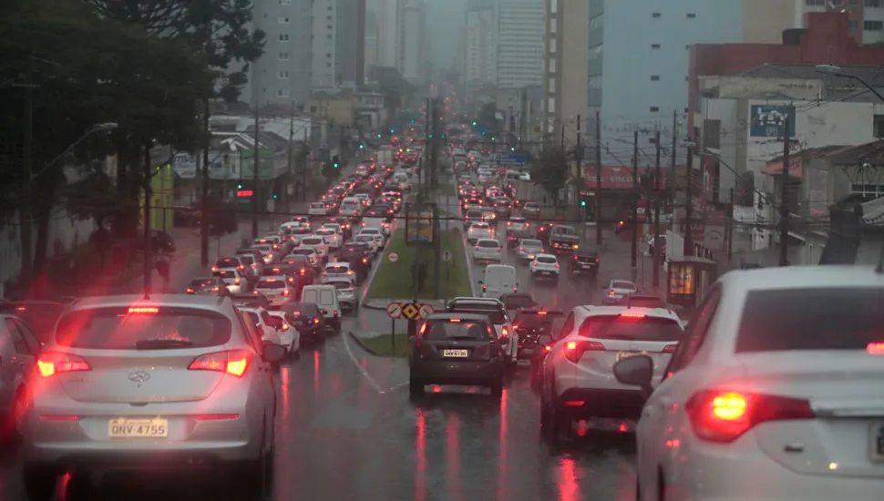 Fotografia de uma avenida movimentada em que as quatro faixas estão congestionadas. No momento da foto, chove.
