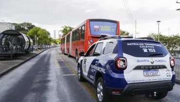 A imagem mostra uma viatura da Guarda Municipal atrás de um biarticulado na canaleta do ônibus.
