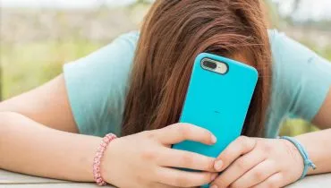 Imagem mostra uma adolescente usando um celular com capinha azul.