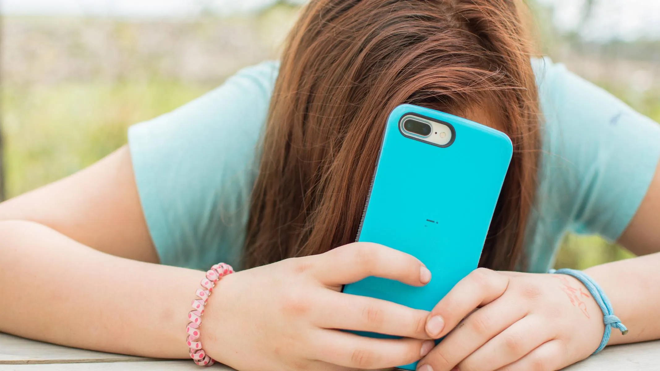 Imagem mostra uma adolescente usando um celular com capinha azul.