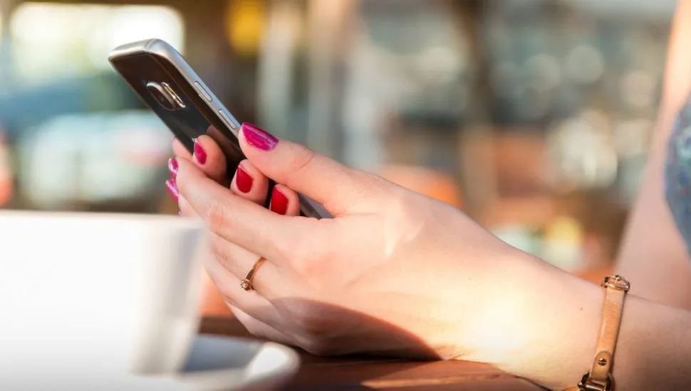 Imagem mostra uma mulher segurando um celular em uma cafeteria.