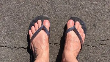 imagem mostra dois pés masculino, com chinelo, pisando no asfalto