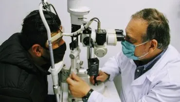 Fotografia de um exame oftalmológico. Há um homem sendo atendido por um médico na imagem.