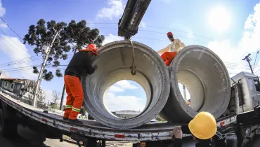 Equipes trabalham no descarregamento de tubos de concreto para as obras de infraestrutura de drenagem e pavimentação da região.