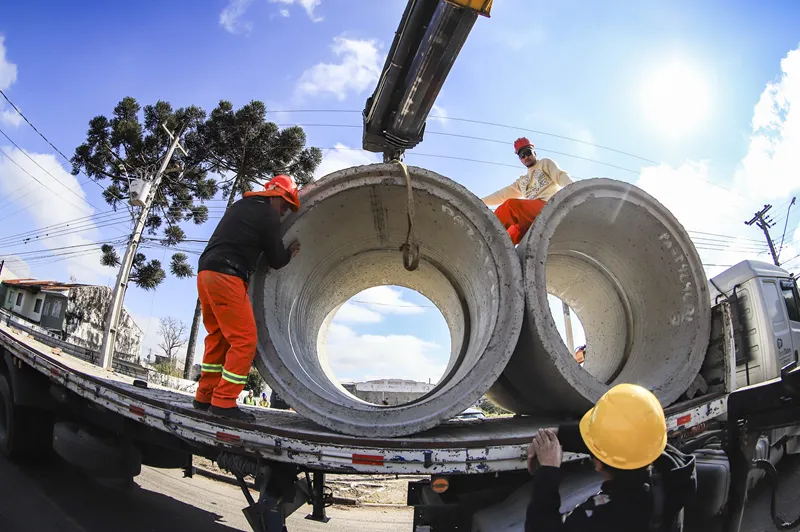 Equipes trabalham no descarregamento de tubos de concreto para as obras de infraestrutura de drenagem e pavimentação da região.