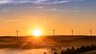 Imagem mostra um campo de energia sustentável. Com o nascer do sol ao fundo e usinas de energia eólica.