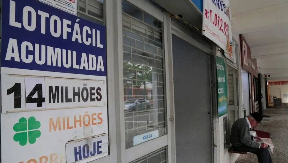 Imagem mostra uma lotérica de Curitiba com um painel informando o prêmio da Lotofácil acumulado em R$ 14 milhões.