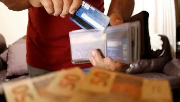 Imagem mostra uma pessoa pegando um cartão de crédito e notas de real.