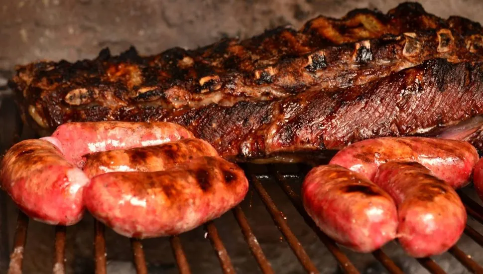 Imagem mostra um churrasco com carne e linguiça na brasa.