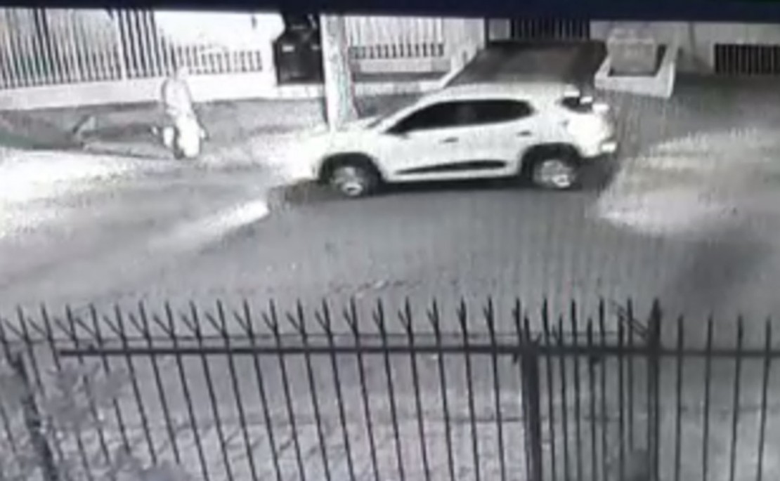 Na sequência, o carro branco, um Renault Kwid, se aproxima e um homem desembarca disparando diversas vezes contra a vítima.