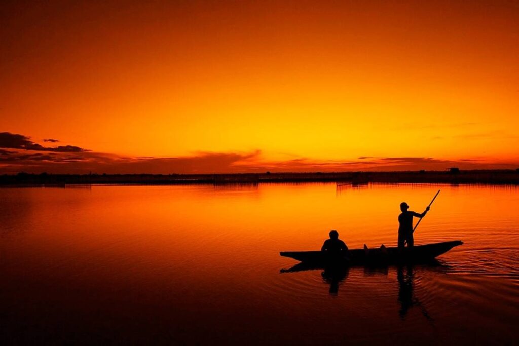 Imagem mostra um barco em um rio no por do sol.