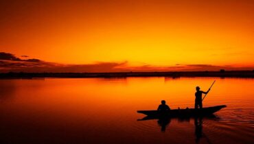 Imagem mostra um barco em um rio no por do sol.