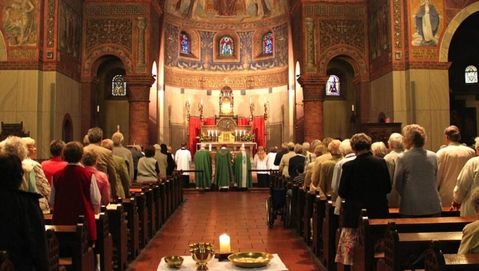 Padre reza missa em uma igreja decorada com luzes em tom amarelado.