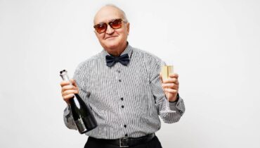 Imagem mostra um idoso rindo com uma champagne e uma taça nas mãos