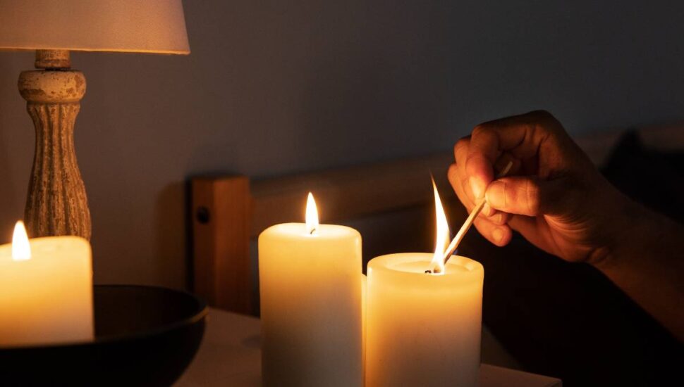 Imagem mostra um apagão e uma pessoa acendendo velas com um fósforo.