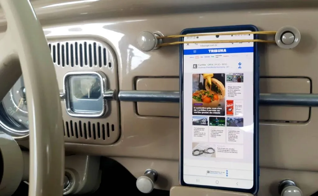 Imagem mostra o painel de um fusca com um celular sendo segurado por um elástico