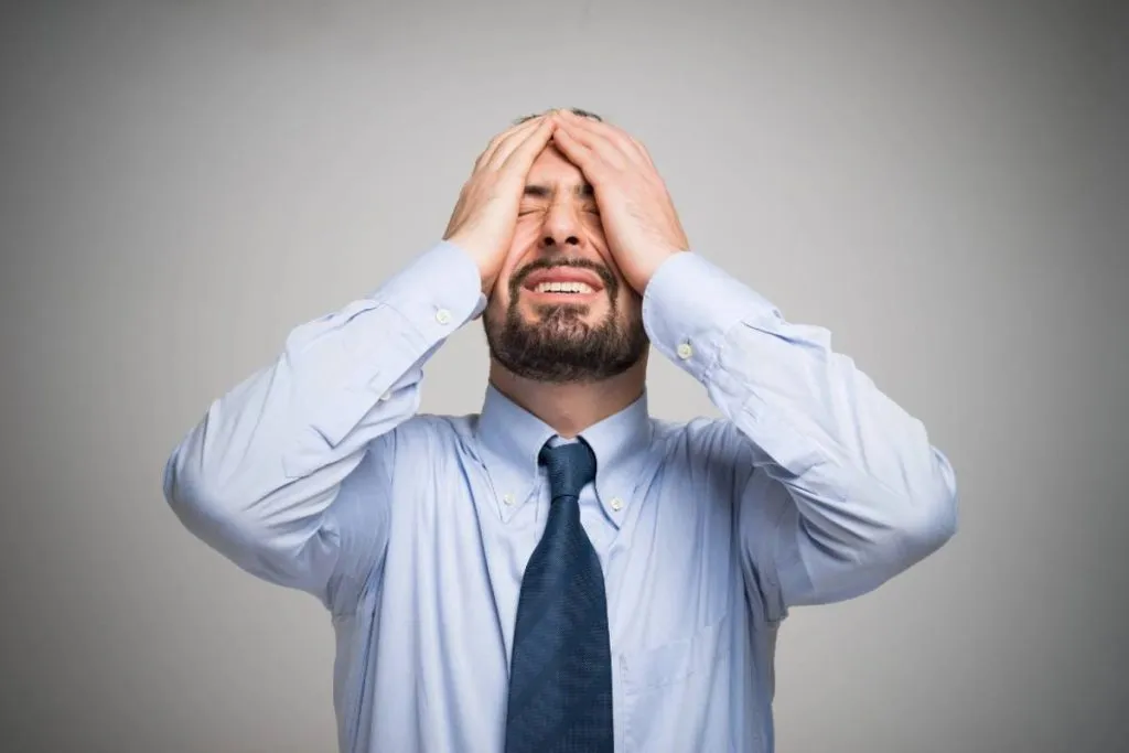 Imagem mostra um homem de camisa azul com grava azul se lamentando com as mãos na cabeça