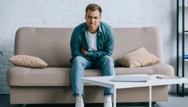 Imagem mostra um homem com dor de barriga em um sofá