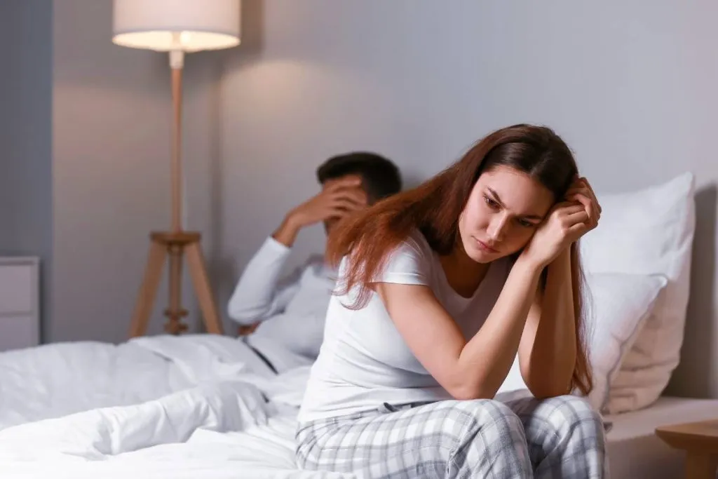 Imagem mostra um casal em uma cama e ela com cara de desapontada