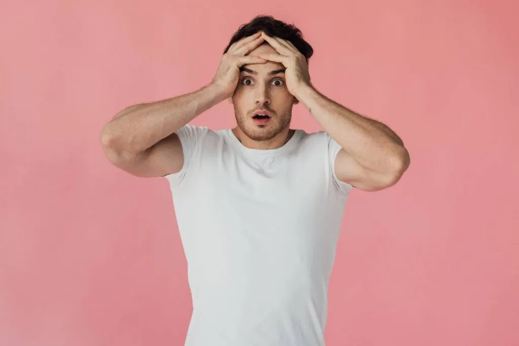 Imagem mostra um homem de camiseta branca com a mão na cabeça desesoerado.
