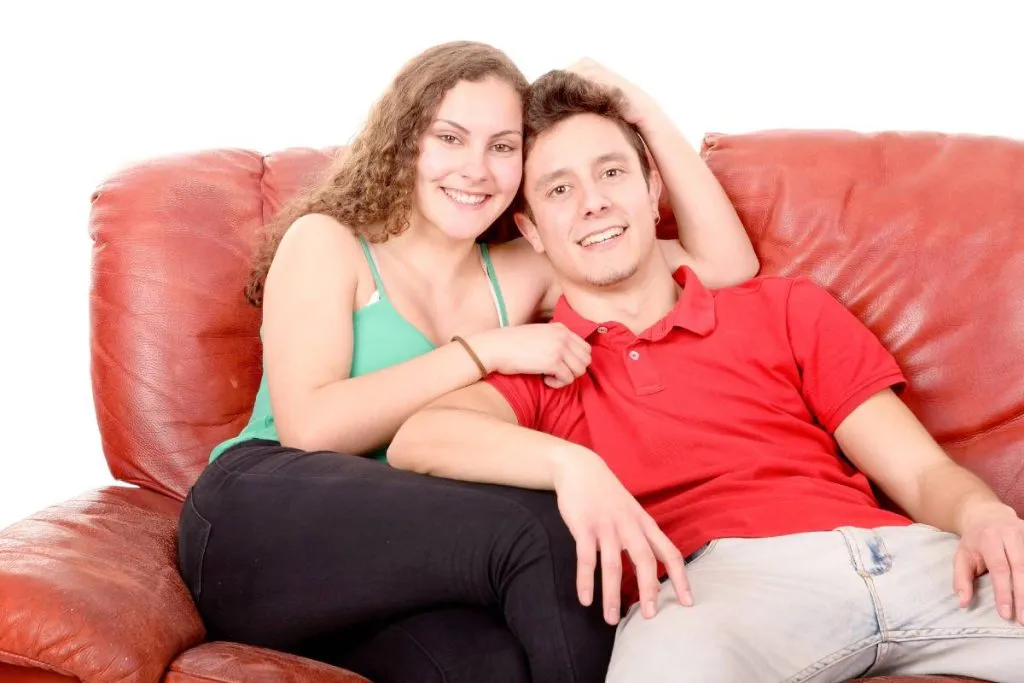 Imagem mostra um casal sentado em um sofá vermelho.