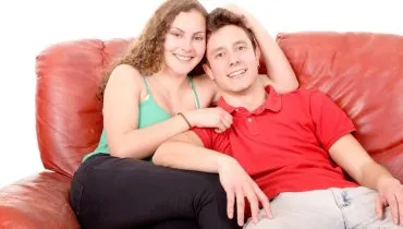 Imagem mostra um casal sentado em um sofá vermelho.