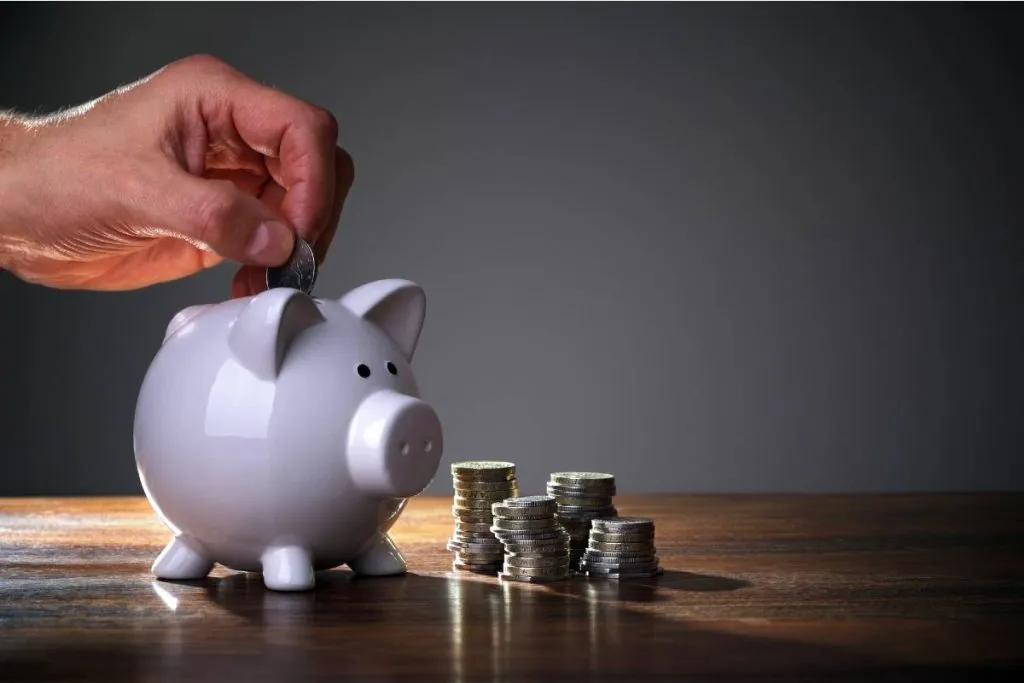 Imagem mostra um homem colocando moedas em um cofrinho em formado de porco.