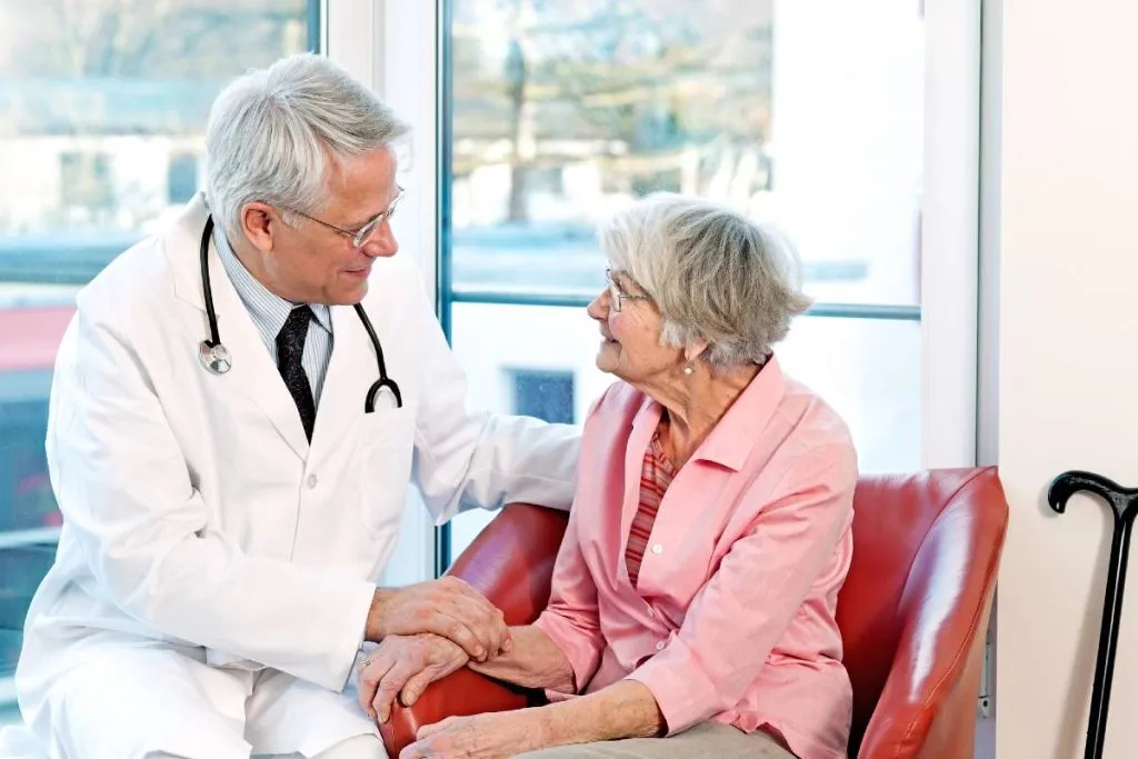 Imagem mostra uma idosa conversando com um médico.